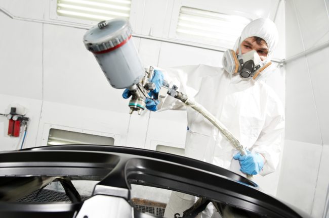 Auto painter wearing full respirator and protective suit while spray painting a vehicle panel